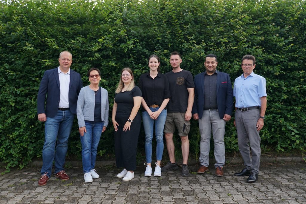 Mittig im Bild steht das gesamte Team, bestehend aus sieben Mitarbeitern.